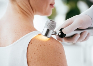 Dermatologist - Dermatologist examining shoulder skin with dermatoscope during check-up.
