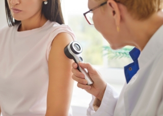 Dermatologist - Dermatologist examining shoulder/arm skin with dermatoscope during check-up.